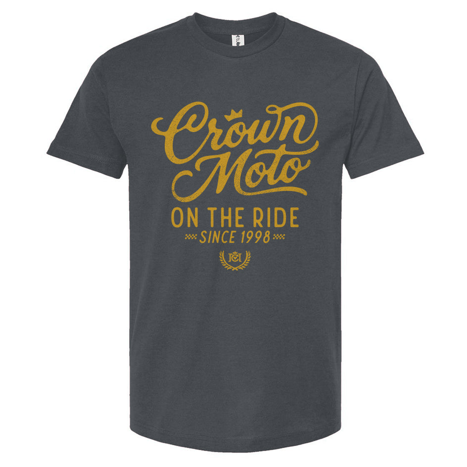 A dark gray crewneck t-shirt with a gold graphic print on the front reading 'Crown Moto ON THE RIDE SINCE 1998' on a plain white background.