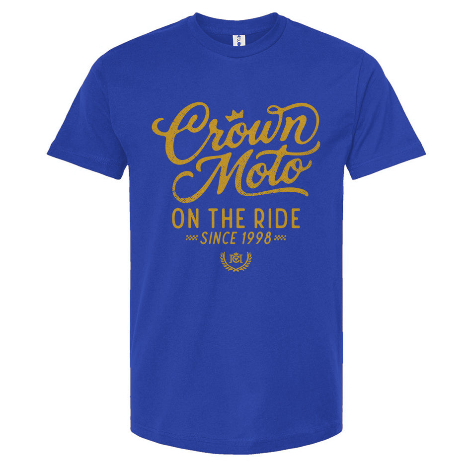 A royal blue short-sleeve t-shirt with a gold graphic print on the front reading 'Crown Moto ON THE RIDE SINCE 1998' on a plain white background.