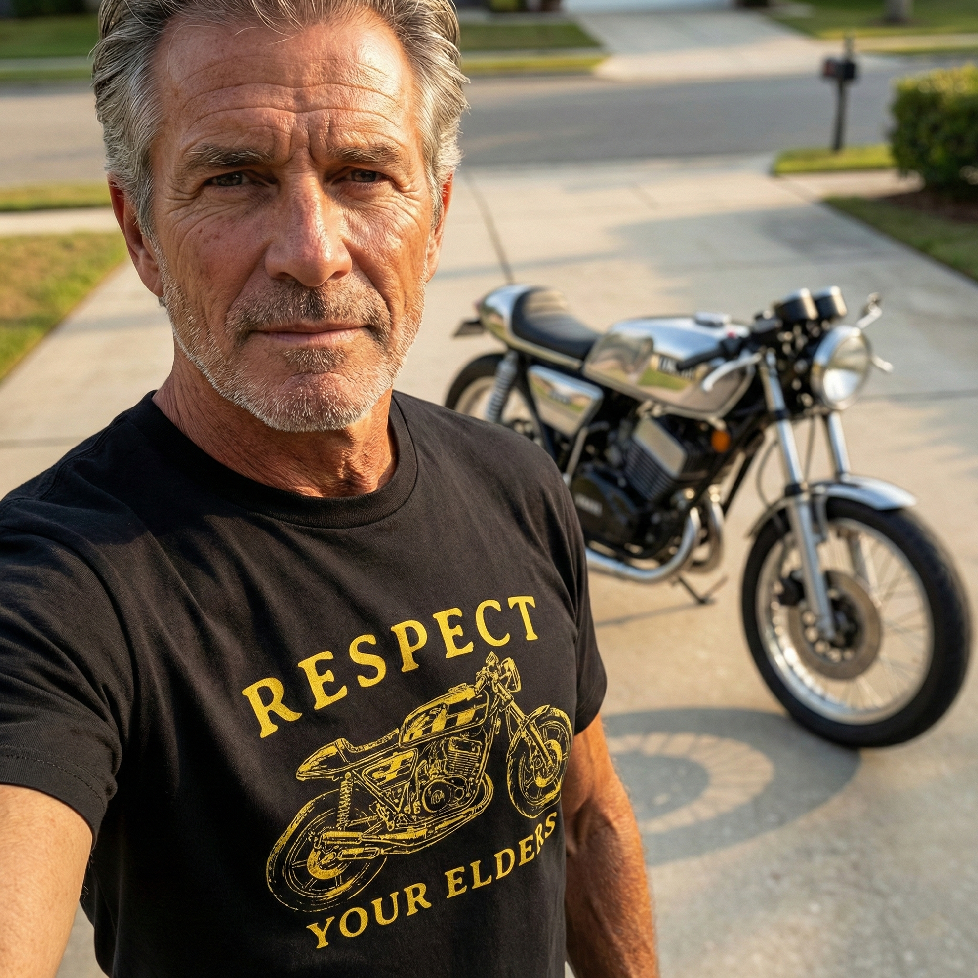 Man wearing a black t-shirt with a vintage RD400 motorcycle graphic and 'respect your elders' text, standing in front of a motorcycle.