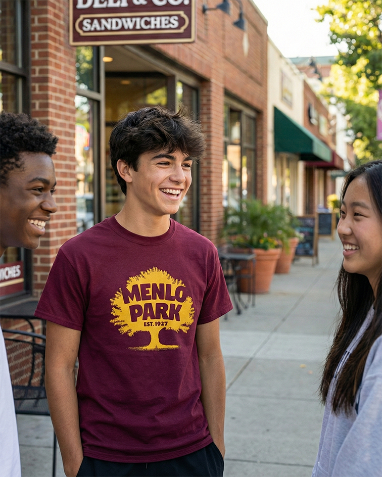 Teenagers standing and talking on a sidewalk with the one in the middle wearing a Menlo Park Est. 1927 maroon and gold t-shirt