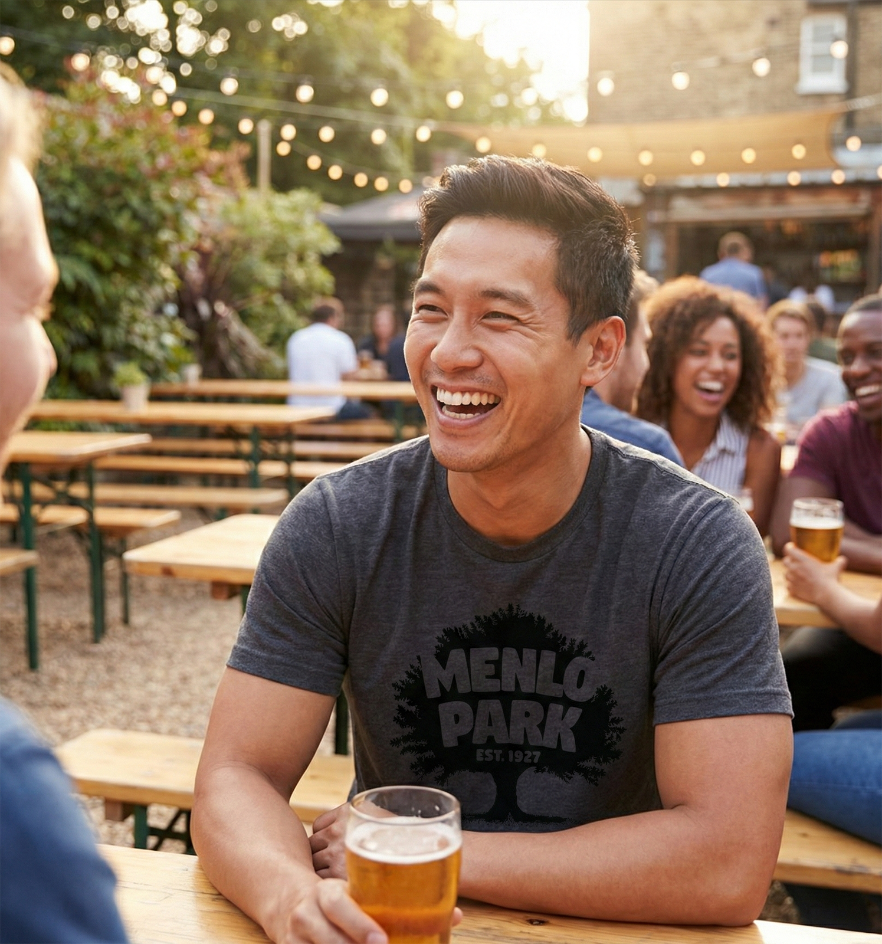 Man wearing a Menlo Park 1927 heather charcoal t-shirt sitting with friends at an outdoor beer garden