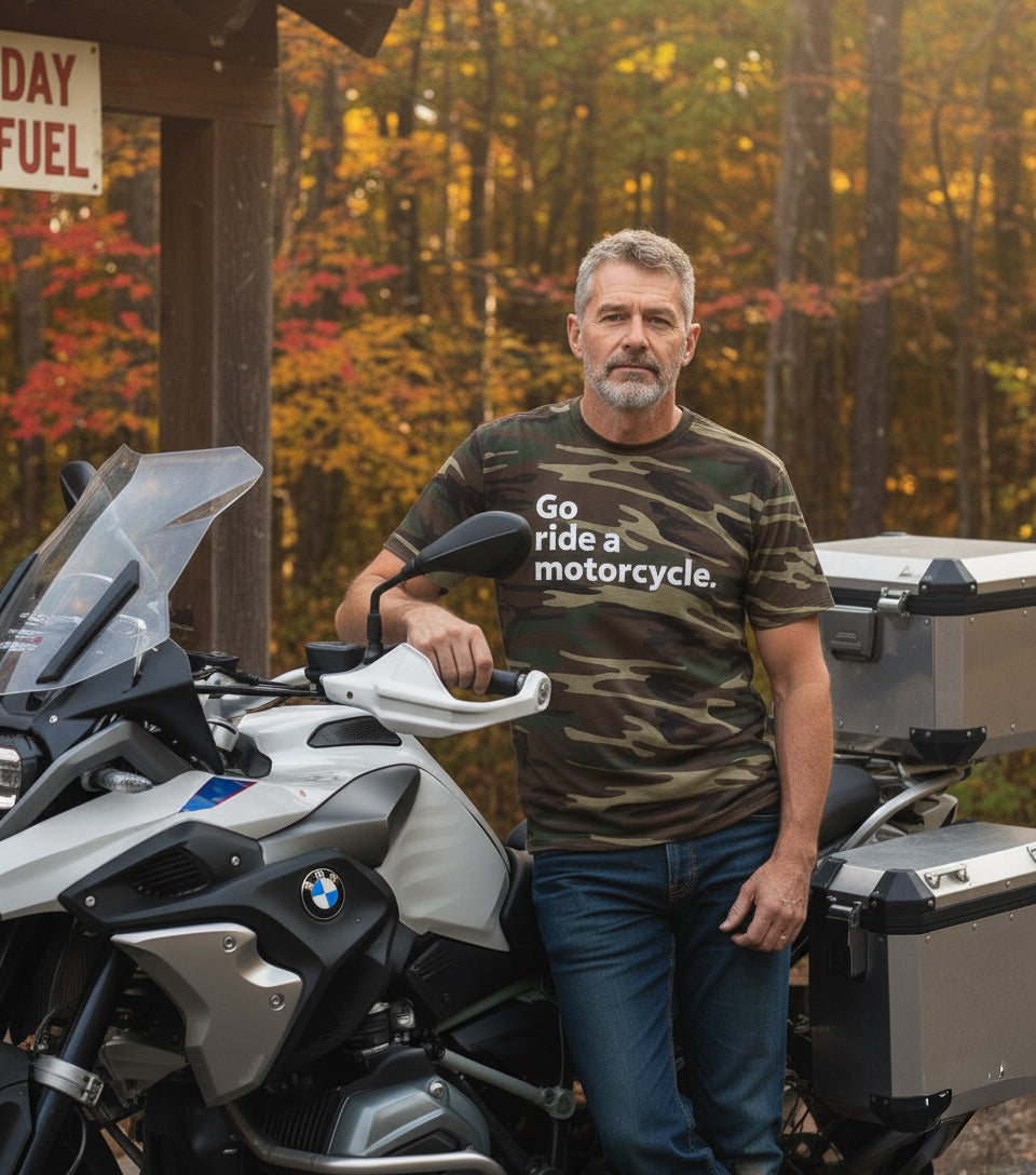 Man standing next to a motorcycle with 'Go ride a motorcycle' camouflage t-shirt in a forest setting