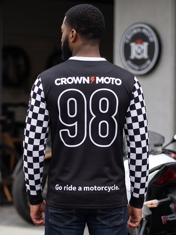 A man viewed from behind wearing a black long-sleeve jersey with black-and-white checkered sleeves. The back features 'CROWN MOTO' in white text with a red lightning bolt, the number '98' in large white outline numerals, and the phrase 'Go ride a motorcycle.