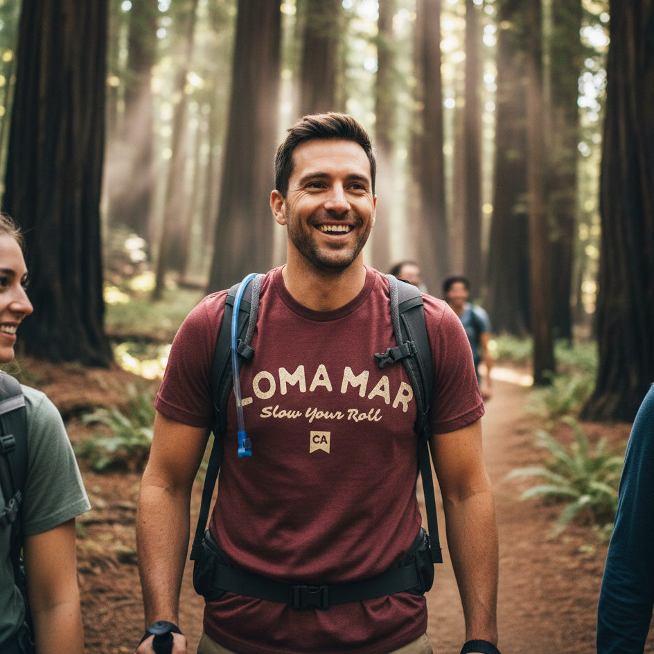 Man hiking in a forest wearing a maroon t-shirt with 'Loma Mar' branding.