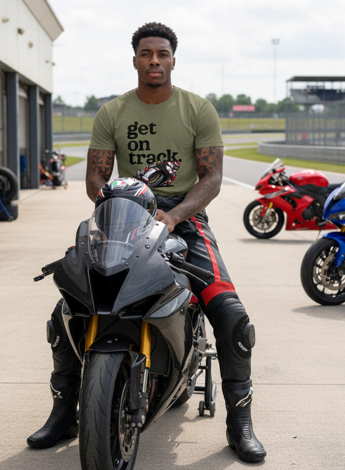 Man sitting on a sportbike motorcycle wearing a Get on track" t-shirt from Crown Moto with a racetrack and motorcycles in the background