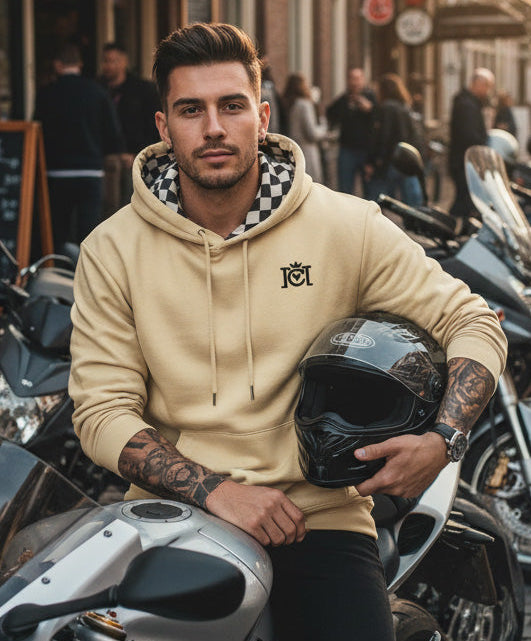 Man sitting on a motorcycle in the city wearing the Crown Moto Checkered Flag Embroidered Logo Hoodie in Old Gold color