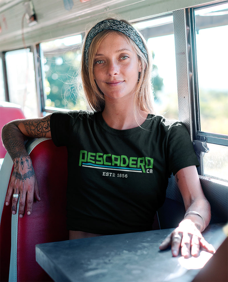 Woman sitting in a bus wearing a short sleeve t-shirt with original Pescadero design printed across the chest