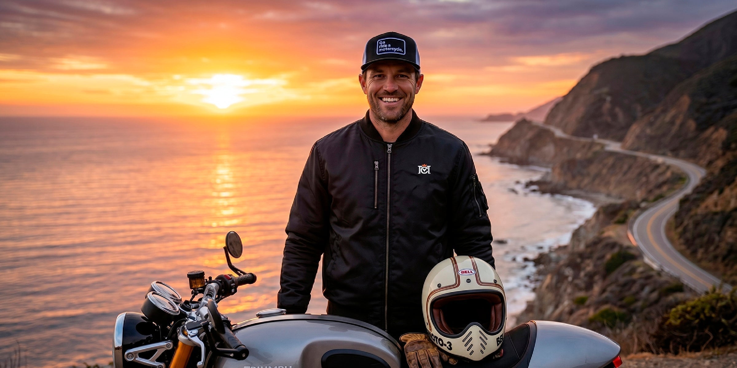 man wearing crown moto armored bomber jacket posing with his motorcycle on the coast during sunset