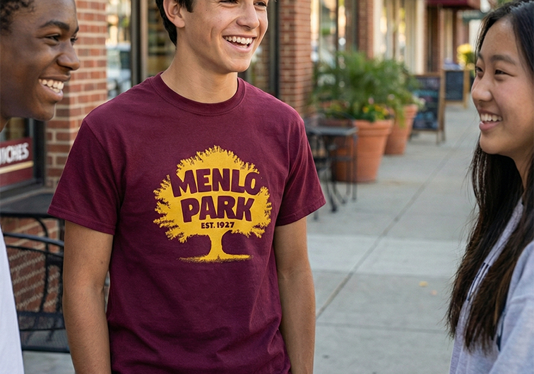 Teenage boy wearing a Menlo Park 1927 t-shirt talking with friends on a downtown sidewalk
