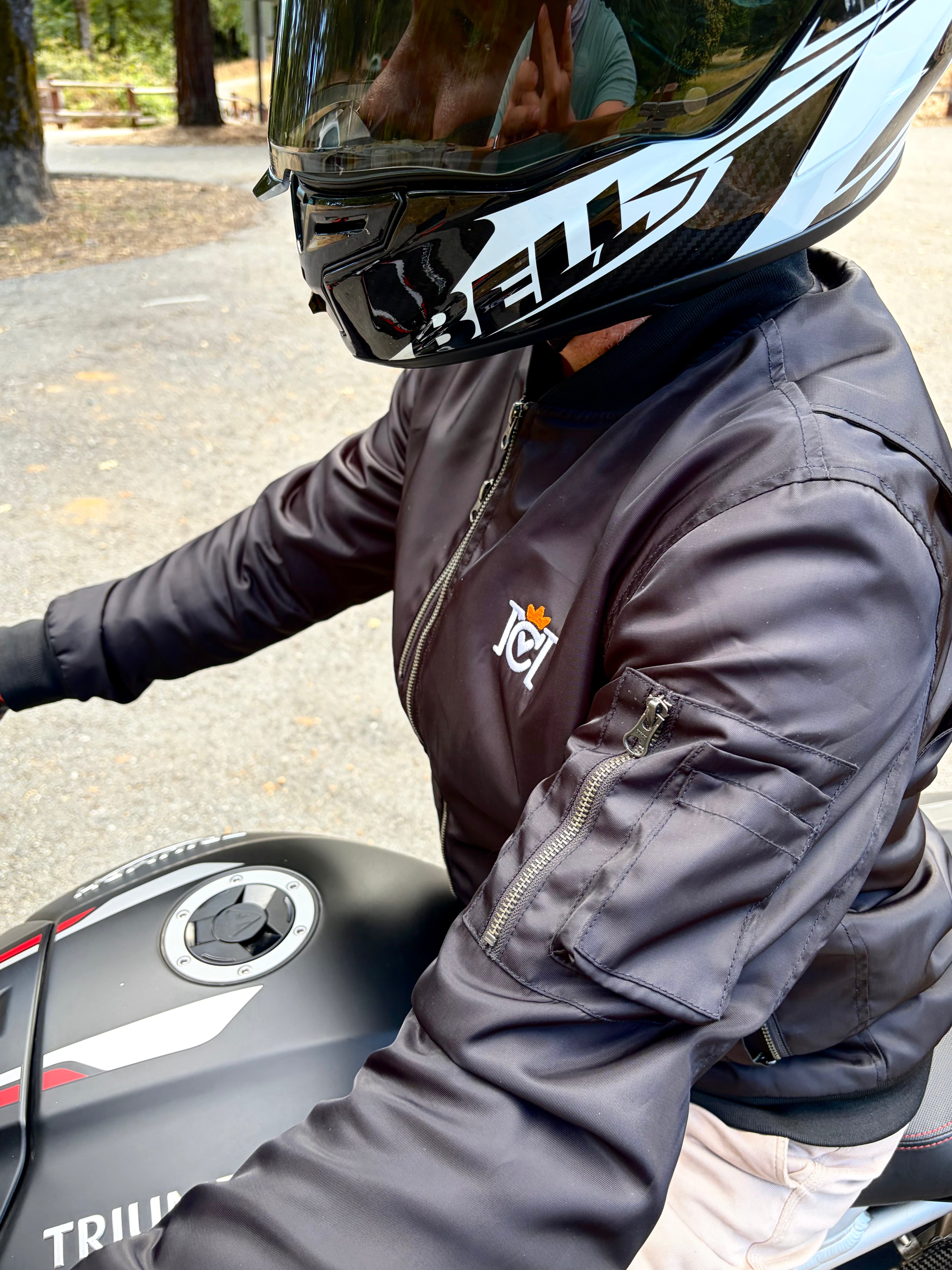 Rider wearing a Crown Moto armored bomber jacket sitting on a triumph motorcycle with helmet on