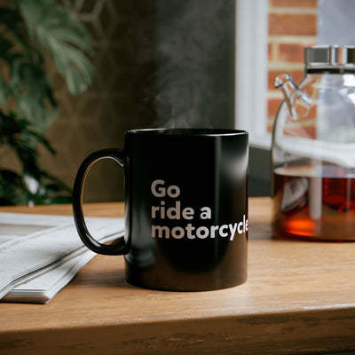 Go ride a motorcycle black coffee mug sitting on a desk with steam coming from the top