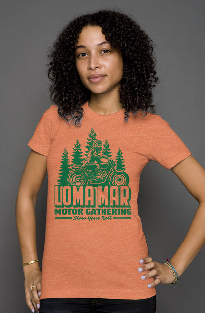 Woman wearing orange short sleeve t-shirt with original Loma mar motor gathering scrambler motorcycle design on chest in green