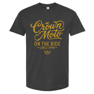 Indigo blue short-sleeve t-shirt with a gold graphic print on the front reading 'Crown Moto ON THE RIDE SINCE 1998' on a plain white background.