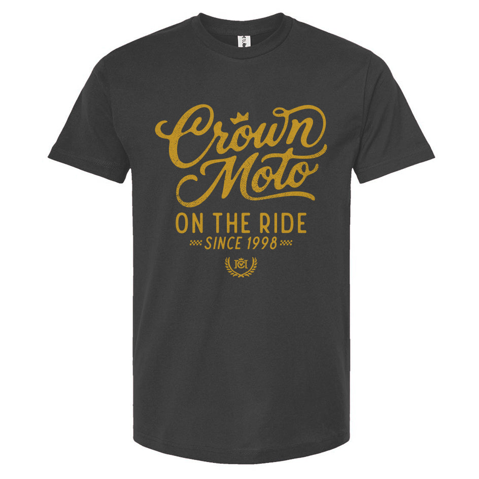 Indigo blue short-sleeve t-shirt with a gold graphic print on the front reading 'Crown Moto ON THE RIDE SINCE 1998' on a plain white background.
