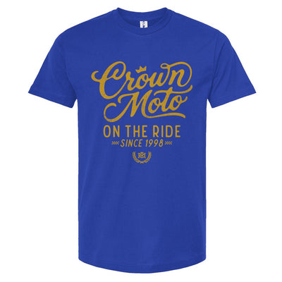 A royal blue short-sleeve t-shirt with a gold graphic print on the front reading 'Crown Moto ON THE RIDE SINCE 1998' on a plain white background.