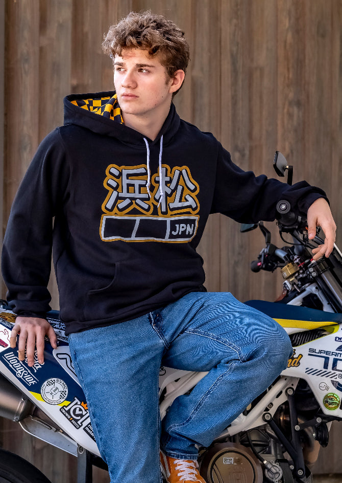 young man sitting on a motorcycle wearing black Hamamatsu JPN hoodie with black and yellow checker lined hood