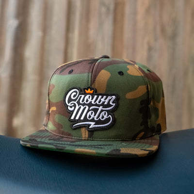 crown moto script patch on front of green camouflage yupoong snapback hat, motorcycle lifestyle brand, flat brim, premium quality hat, hats for motorcyclists, logo, motorbikes, motorcycles
