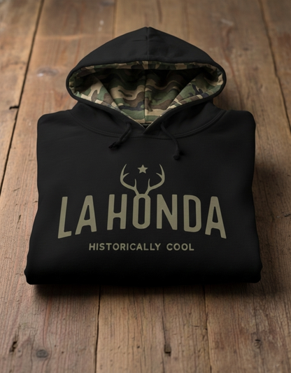 Black hoodie with camouflage lined hood 'LA HONDA HISTORICALLY COOL' text on a wooden surface
