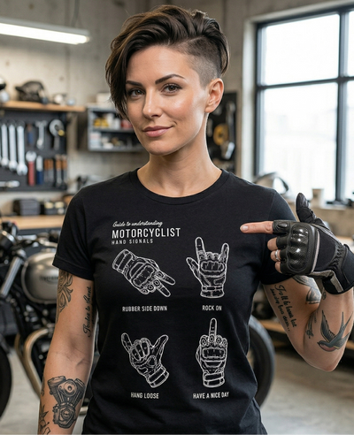 Pretty woman with a modern haircut wearing a Motorcyclist Hand Signals t-shirt standing in a garage with a motorcycle in the background