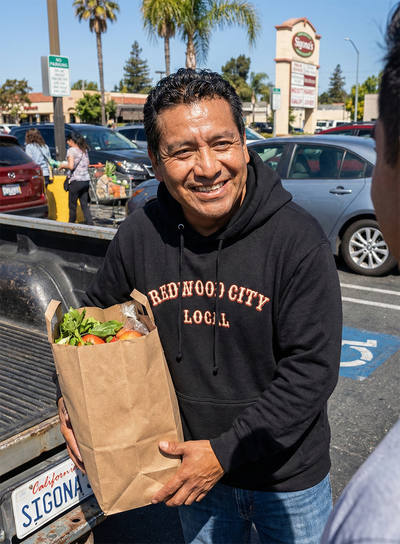 Man wearing a Redwood City Local hoodie loading groceries into his truck and smiling