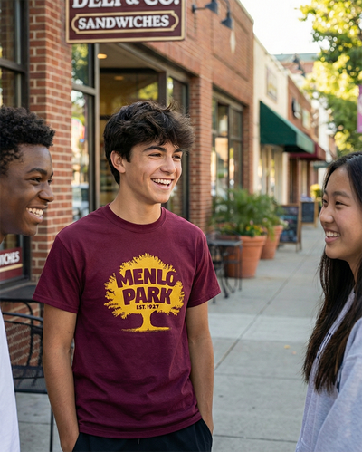 Teenagers standing and talking on a sidewalk with the one in the middle wearing a Menlo Park Est. 1927 maroon and gold t-shirt