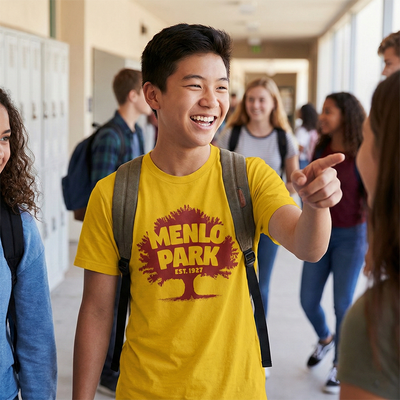 Young man in a yellow 'Menlo Park' shirt pointing in a school hallway with other students.