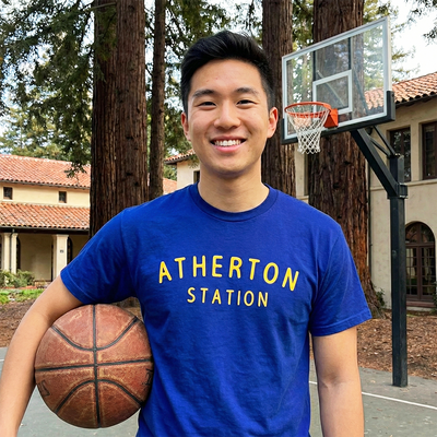 young man wearing a blue 'Atherton Station' t-shirt holding a basketball on a court