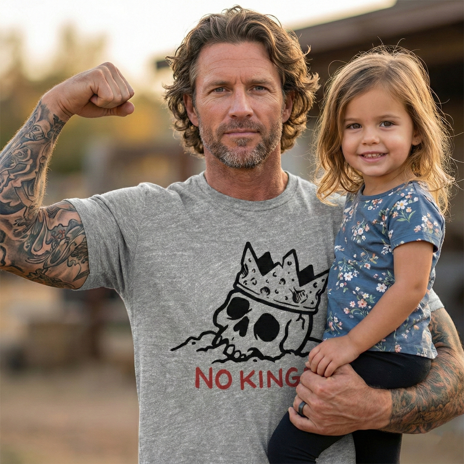 Man wearing a NO KINGS t-shirt holding his young daughter in his arms