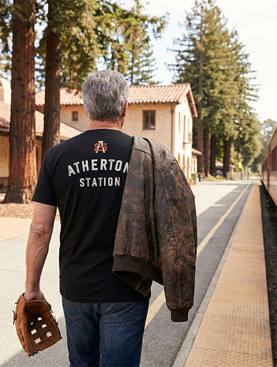 Man wearing a black t-shirt with 'Atherton Station' on the back, standing on a train platform.