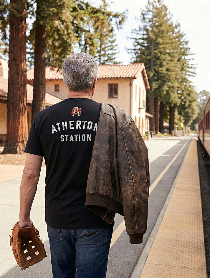Man wearing a black t-shirt with 'Atherton Station' on the back, standing on a train platform.