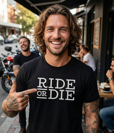 Man wearing a black t-shirt with 'Ride or Die' text, pointing at himself, in an urban setting.