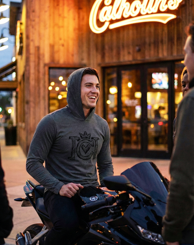 Man sitting on a motorcycle in front of a restaurant wearing a charcoal grey crown moto sketch hooded jersey