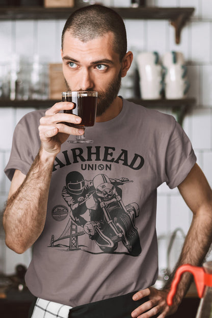 Man drinking from a glass while wearing a 'Airhead Union' t-shirt in a kitchen setting.