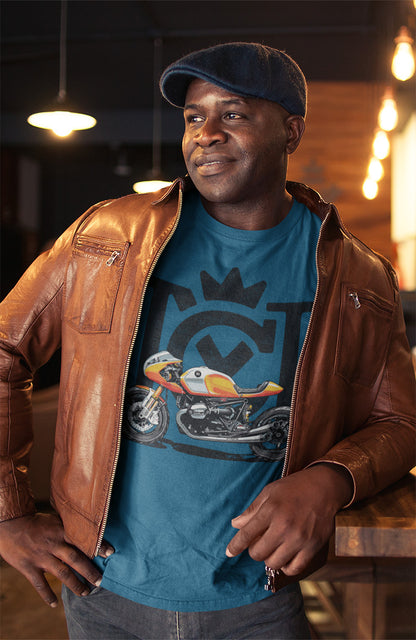 Man leaning on a bar wearing a paperboy cap and leather jacket and Crown Moto Cafe Racer t-shirt with image of custom BMW Cafe Racer motorcycle