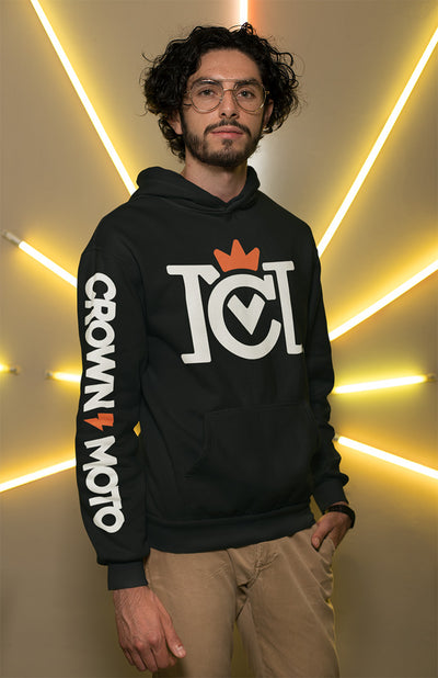 Man wearing a black Crown Moto Factory Team hoodie with chest and sleeve printing, standing in front of cool lighting
