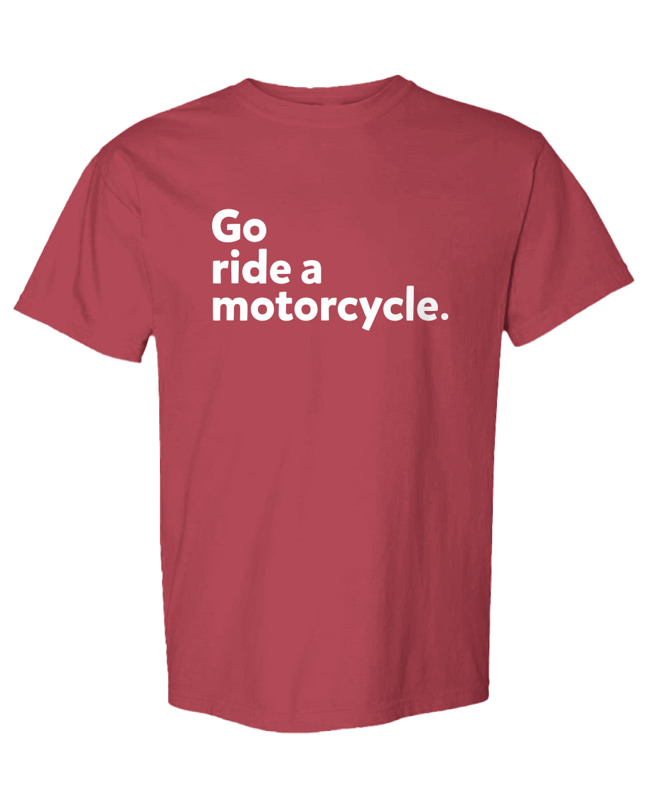 A short-sleeve crewneck t-shirt in a dusty rose red color, featuring the phrase 'Go ride a motorcycle.' printed in white sans-serif text across the chest