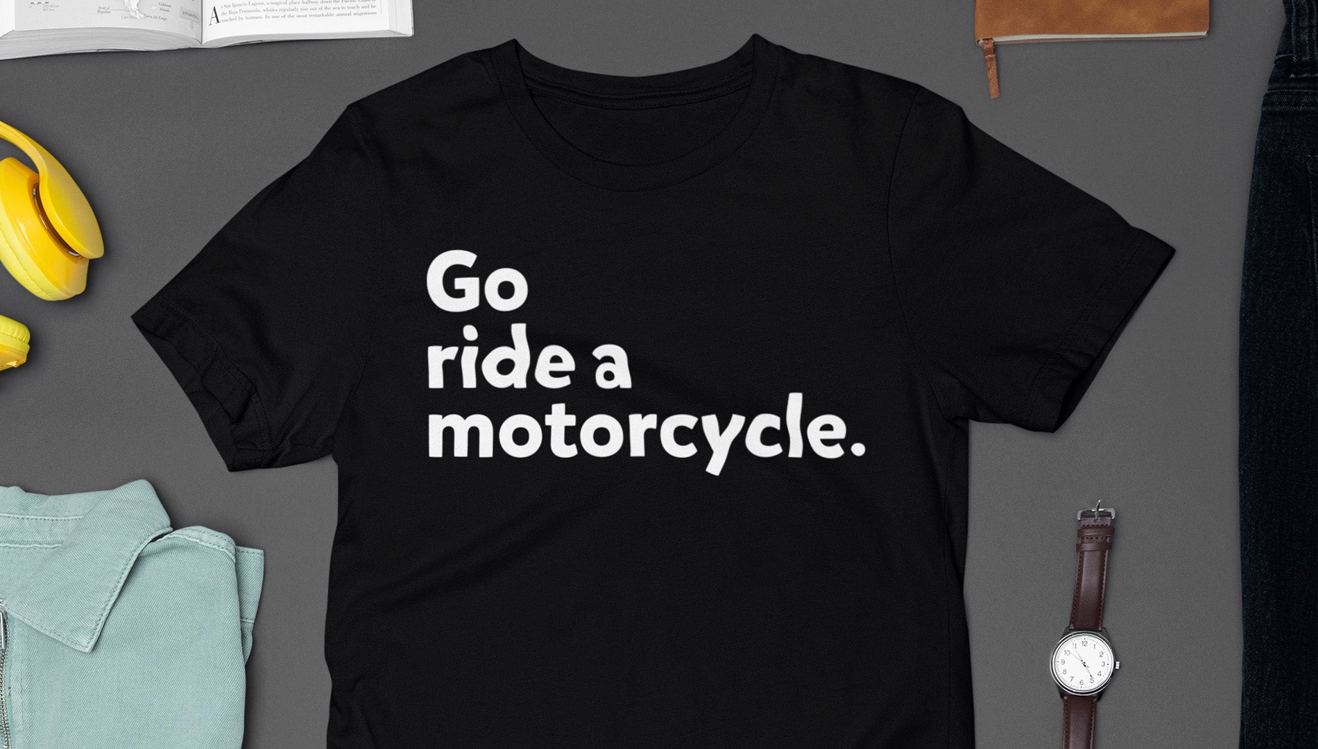 Black t-shirt with 'Go ride a motorcycle' text on a gray surface with casual items.