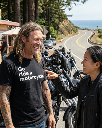 Long haired man wearing a "Go ride a motorcycle" shirt by Crown Moto talking to a woman who is pointing at his shirt and smiling