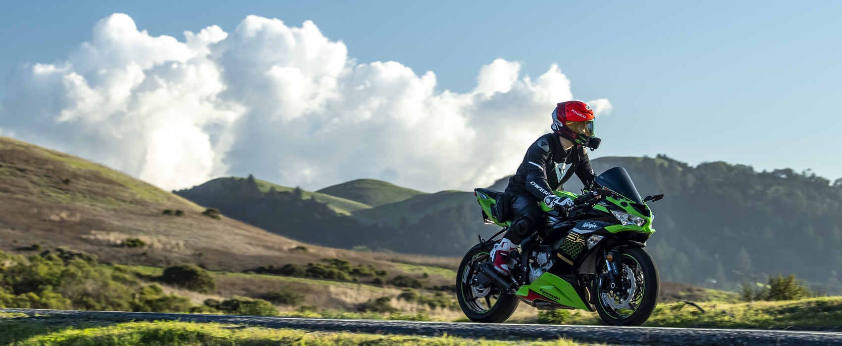 photograph taken by Crown Moto of man on Kawasaki motorcycle riding on skyline blvd in woodside california with blue skies, white clouds and green hills in the background