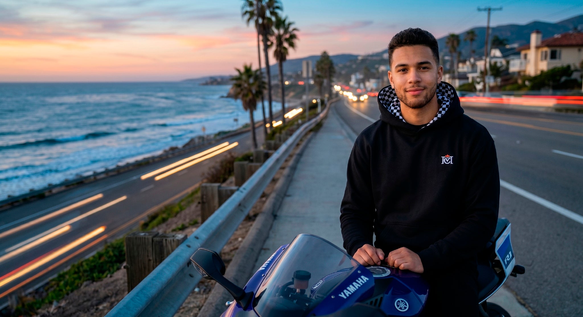 Man wearing crown moto armored hoodie sitting on a motorcycle overlooking the ocean