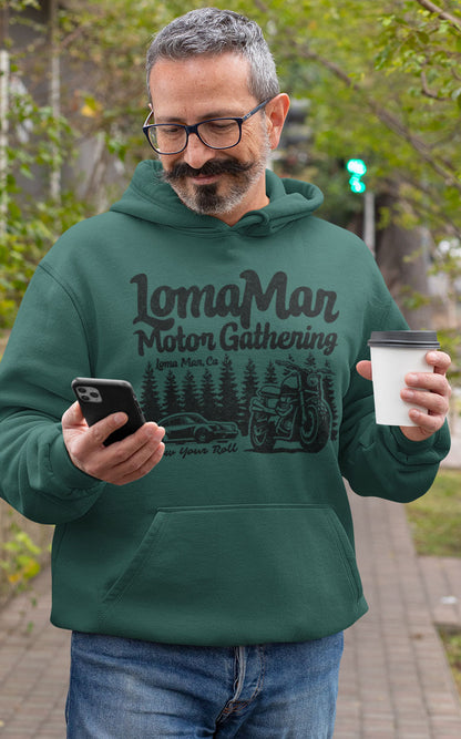 Man looking at phone wearing a green hooded sweatshirt with "Loma Mar Motor Gathering" design on chest