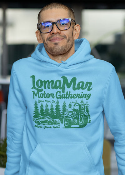 Man smiling wearing light blue hooded sweatshirt with "Loma Mar Motor Gathering" design in green on chest