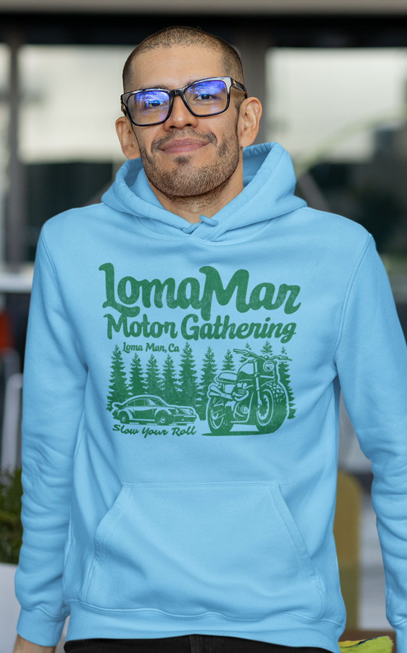 Man smiling wearing light blue hooded sweatshirt with "Loma Mar Motor Gathering" design in green on chest