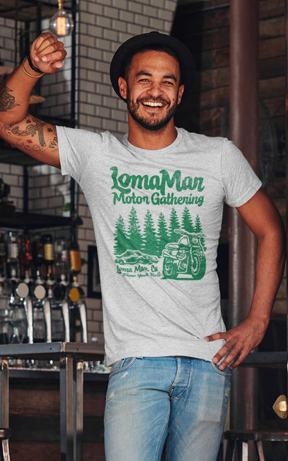 Man standing in doorway smiling wearing a grey short sleeve t-shirt with "loma mar motor gathering" design in green on chest