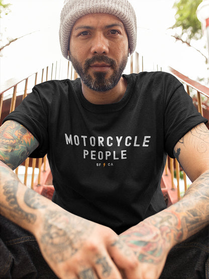 Man sitting on steps wearing a beanie and a black t-shirt with "Motorcycle People" SF CA design on chest