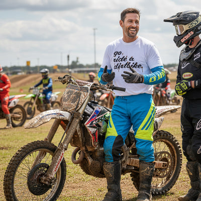Man on a dirt bike with 'go ride a dirtbike' shirt at an outdoor motocross track.