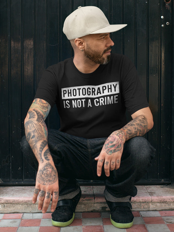 Man sitting wearing hat and short sleeve t-shirt with "photography is not a crime" on chest