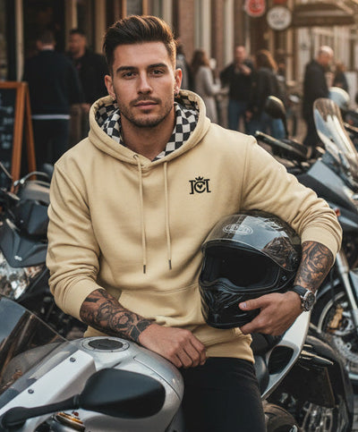 Man sitting on a motorcycle in the city wearing the Crown Moto Checkered Flag Embroidered Logo Hoodie in Old Gold color