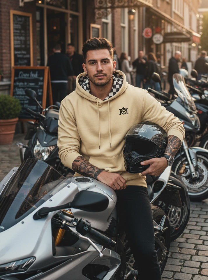 Man sitting on a motorcycle in the city wearing the Crown Moto Checkered Flag Embroidered Logo Hoodie in Old Gold color