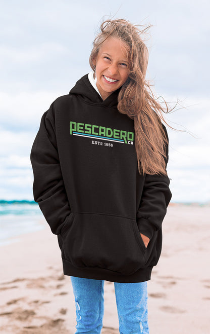 Woman smiling at the beach wearing a hooded sweatshirt with original Pescadero design printed across the chest